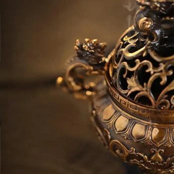 Close-up of an ornate brass teapot with intricate gold scrollwork and floral filigree, lit warmly against a dark background