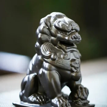 Dark metal Chinese guardian lion (foo dog) statue sitting on a flat base with carved curls of mane.