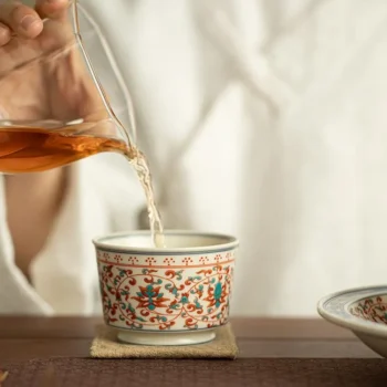 Pouring amber tea into a decorative ceramic cup on a wooden table.